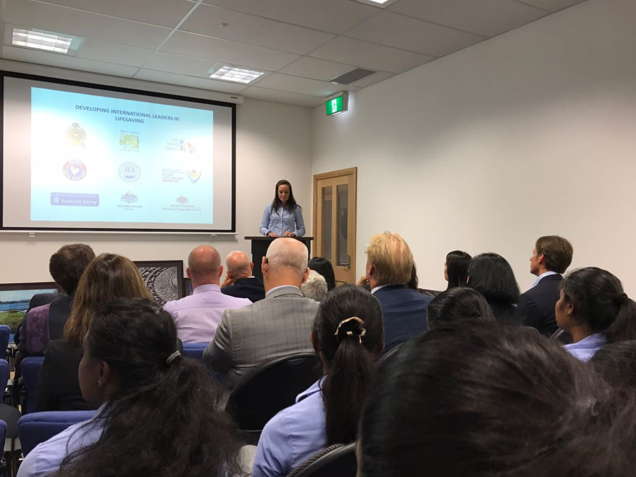 Person presenting at a lectern with people watching on